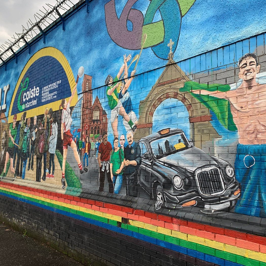 Failte Feriste Mural Divis Street Colourful mural depicting people celebrating with a black taxi and various community scenes.
